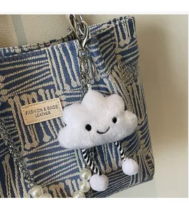Close-up of white plush cloud pendant with cute smile and pearl chain on canvas bag