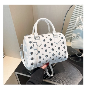 Detail of white Boston bag featuring silver metal rivets and dual handles on a shelf