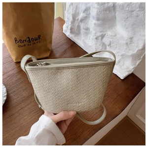 Detail shot of beige woven bucket bag with smooth zipper and brand logo text