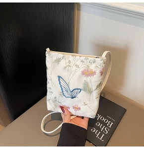 Close-up of white crossbody bag with delicate pink floral and blue butterfly embroidery