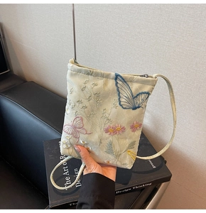 Detailed embroidery of butterflies and flowers on a light green satin crossbody phone bag