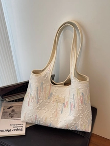Chic cream tote bag with colorful wave embroidery and waffle texture on a black seat