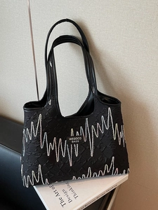 Black pleated tote bag with white wavy stitching and leather handles on white books