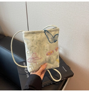 Detailed embroidery of butterflies and flowers on a light green satin crossbody bag