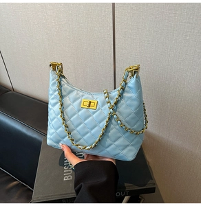 Detail of light blue quilted shoulder bag featuring gold chain and metallic turn-lock closure