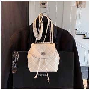 Detail of white quilted backpack featuring chain straps and metallic turn-lock closure