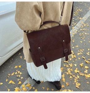 Deep brown vintage messenger bag with metal buckles and handle on autumn street