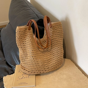 Close-up of woven straw tote bag with brown faux leather straps on a minimalist stone
