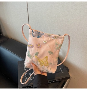 Detail of pink crossbody bag featuring delicate butterfly and daisy embroidery on fabric