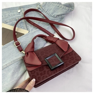 Close-up of burgundy leather crossbody bag featuring leopard print flap and black square buckle