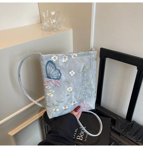 Detail of blue crossbody bag featuring intricate floral and butterfly embroidery patterns