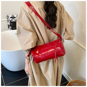 Glossy red patent leather cylinder bag with slender strap shown in a modern lifestyle setting