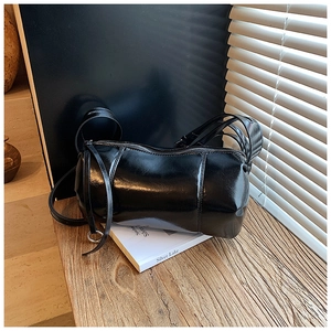 Detail view of black cylinder shoulder bag showing glossy texture and silver metal rings