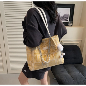 Detail of yellow tote bag featuring pearl chain, plush rabbit charm, and woven texture
