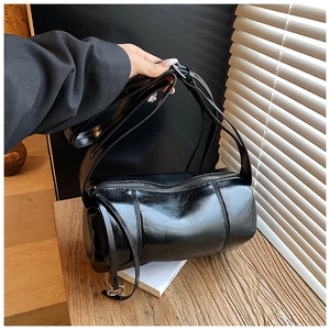Detail showing high-gloss black cylinder bag texture with vertical stitching and zipper