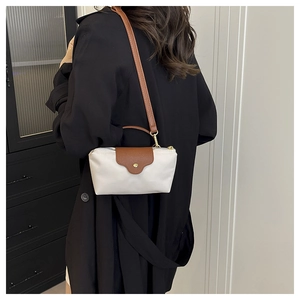 Detail of a nylon crossbody dumpling bag with brown leather strap worn by a model