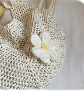 Dettaglio ravvicinato di una borsa in maglia crema con un grande fiore bianco lavorato