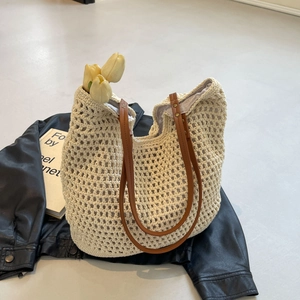 Close-up of beige crochet tote bag with brown leather handles and gold metal rivets