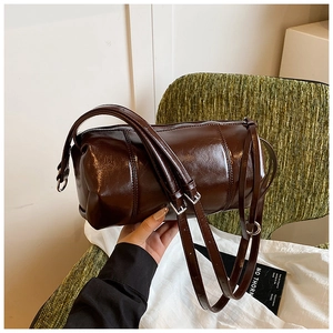 Detail of a deep brown glossy cylinder crossbody bag with fine metallic hardware