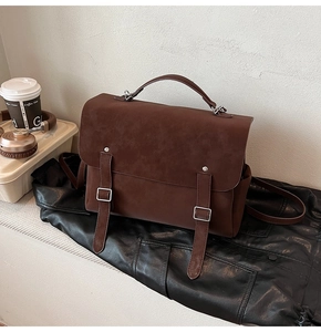 Detail of dark brown matte suede messenger bag with decorative straps and sturdy top handle