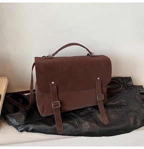 Close-up of vintage brown suede satchel featuring top handle and double buckle straps