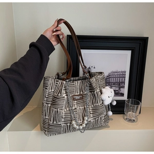 Detail of canvas tote bag featuring geometric patterns, leather handles, and plush charms