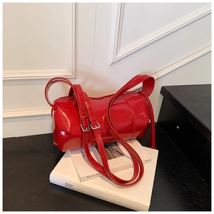 Close-up of a red patent leather cylinder bag with silver buckles on white books