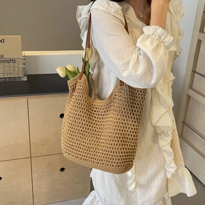 Detail of woven straw tote bag featuring brown leather handles and hollow mesh pattern