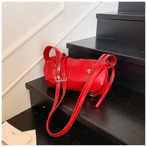 Detail shot of a glossy red cylindrical shoulder bag on a black wooden staircase