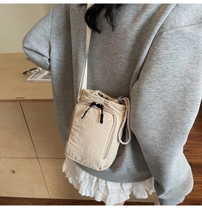 Close-up of beige nylon crossbody bag with drawstring closure and front zipper pocket
