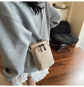 Detail view of a beige nylon crossbody bag with drawstring closure and front zipper pocket