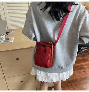 Mini red nylon crossbody bag shown in a professional office setting with a wide shoulder strap