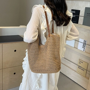 Detail of woven tote bag featuring brown leather shoulder straps and rivet fasteners