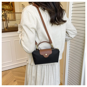Detailed view of a black nylon crossbody bag with brown leather handles on model