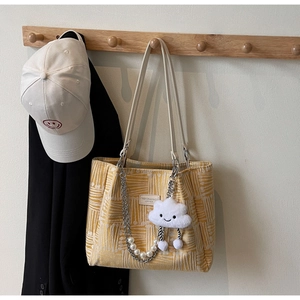 Detail of yellow geometric tote with leather handles, plush charm and pearl chain