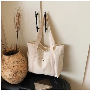 Detailansicht der cremeweißen Canvas-Tasche mit Vordertasche, Metalldruckknopf und Seitenfächern