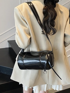 Minimalist black glossy cylinder shoulder bag styled with beige blazer and pleated skirt