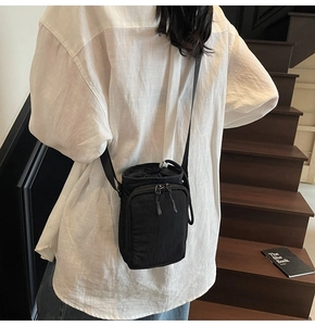 Detail of minimalist black nylon crossbody bag featuring drawstring closure and front zip pocket