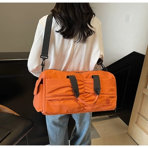 Detailed back view of a large orange nylon travel bag with adjustable strap on a person