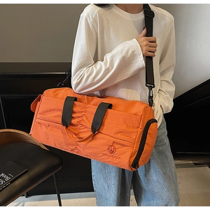 Detail of orange nylon travel bag showing the wrinkled texture and adjustable shoulder strap