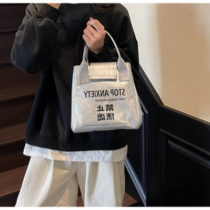 Detail of silver metallic tote bag with black slogan print and crinkled texture