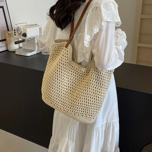Close-up of beige woven tote bag with brown leather straps worn by a model in a cafe