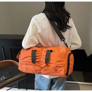 Detail of orange nylon travel bag featuring reinforced black strap and side pleated pocket