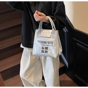 Detail of silver metallic wrinkled paper tote bag featuring bold graphic text and industrial texture