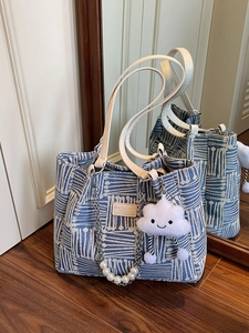 Blue and white woven canvas tote bag with leather straps and pearl charm in a room setting