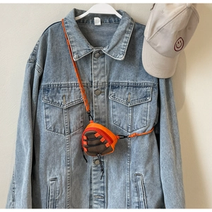 Macro shot of an orange triangular crossbody mini bag hanging on a denim jacket