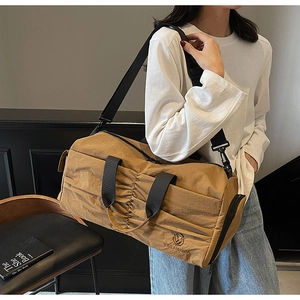 Detail of khaki nylon travel bag featuring unique pleated design and brand embroidery