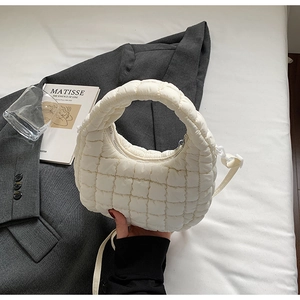 Gros plan du sac bandoulière matelassé beige tenu à la main sur une tenue grise