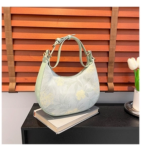 Detailed close-up of a floral print half-moon hobo bag on a book with a wooden background