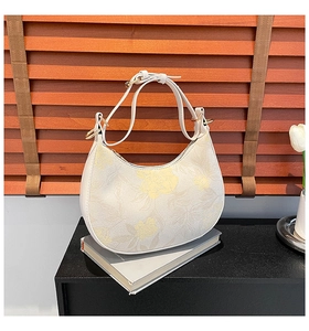 Detail of floral crescent shoulder bag with white leather strap on dark wooden background